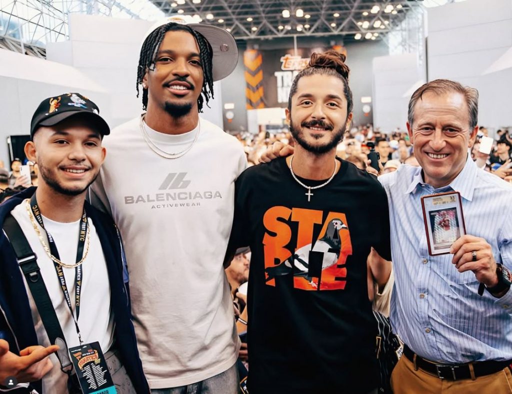 Commanders-Managing Partner Josh Harris (ganz rechts) hält die Jayden-Daniels-Rookie-Karte in die Kamera, neben ihm Verkäufer Josh Roth (mitte rechts), NFL-Star Jayden Daniels (mitte links) und ein weiterer Miteigentümer der Karte (ganz links) – aufgenommen beim Fanatics Fest 2025 nach dem spektakulären $500.000-Deal.