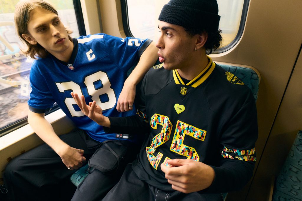Zwei Personen sitzen in der Berliner S-Bahn, eine trägt ein Indianapolis-Colts-Trikot, die andere das neue NFL Berlin Game Fan-Trikot von NFL, Fanatics und BVG.