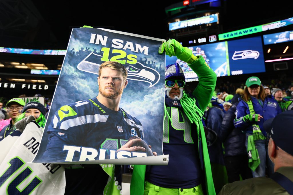 Seattle Seahawks jubeln nach dem Einzug in den Super Bowl – im Hintergrund ein augenzwinkernder Verweis auf die „göttliche Serie“, die Seattle immer dann erreicht, wenn im Vatikan weißer Rauch aufsteigt.