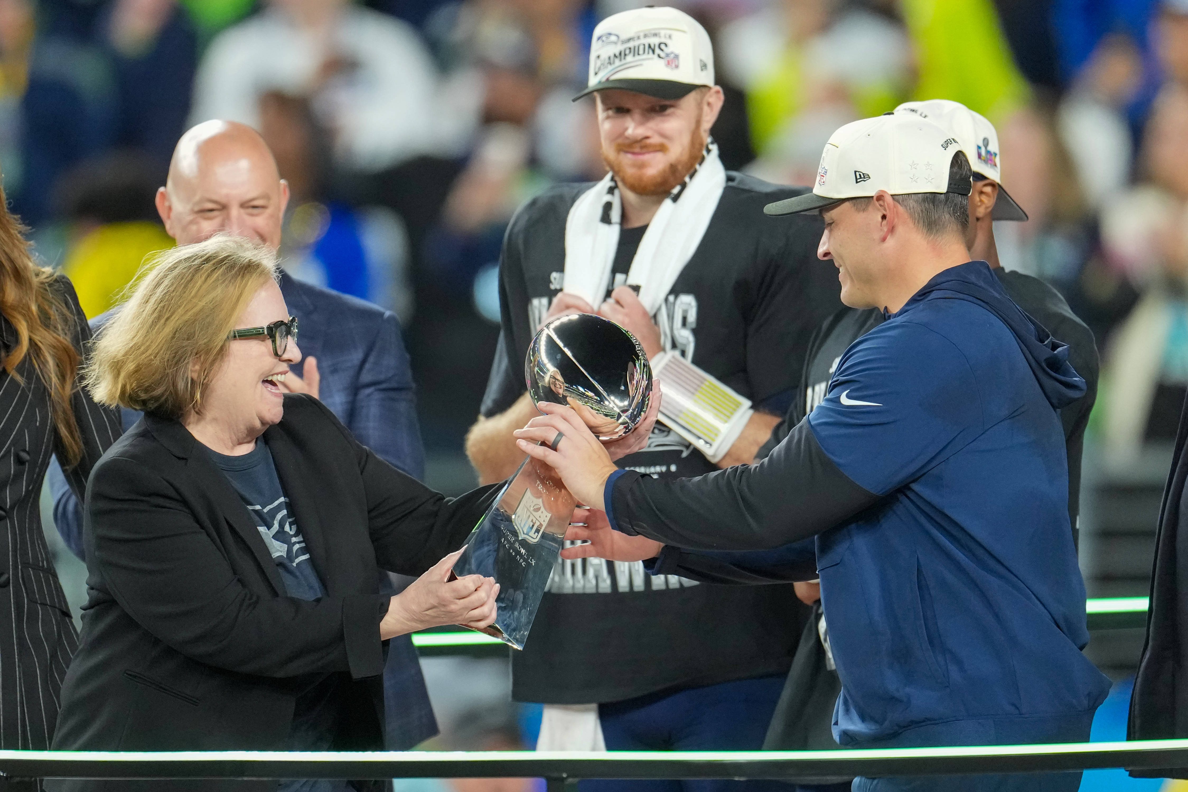 Noch-Vorsitzende der Seattle Seahawks, Jody Allen (l.), übergibt die Vince-Lombardi-Trophy an Head Coach Mike Macdonald (r.) – beobachtet von Quarterback Sam Darnold (m.).
